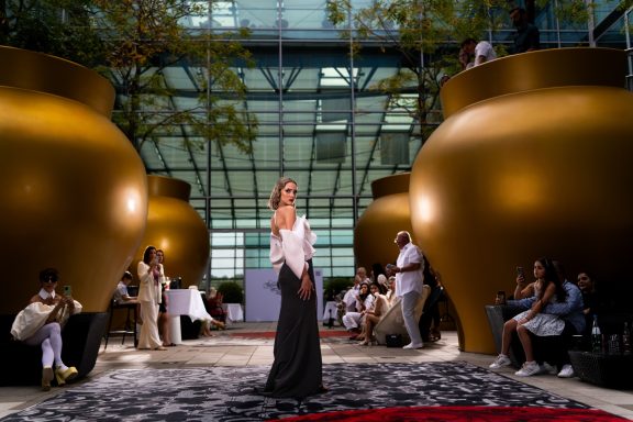 Frau in eleganter Kleidung posiert vor großen goldenen Töpfen in einem modernen Innenraum.